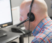 Thumbnail for Man using Koss CS200-USB headset at desk, ideal for schools, clarity in education, bulk headphone pack for learning.