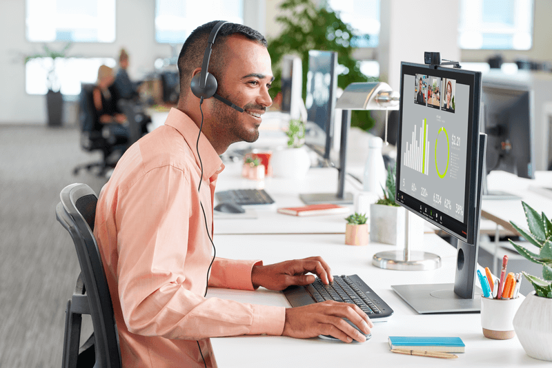 Smiling man uses Logitech H340 USB headset for clear calls and music in a modern office setting, ideal for education.