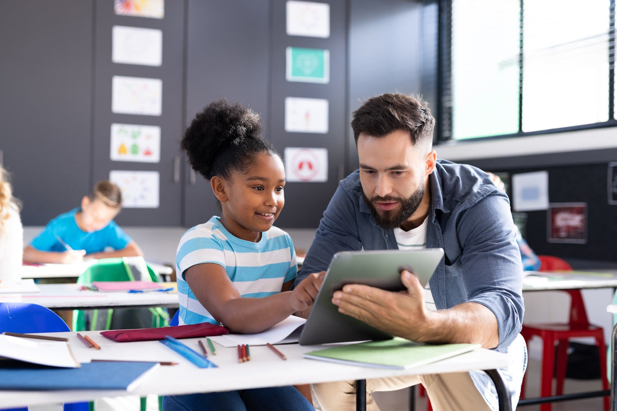 Teacher helping a student use a tablet during a classroom learning activity