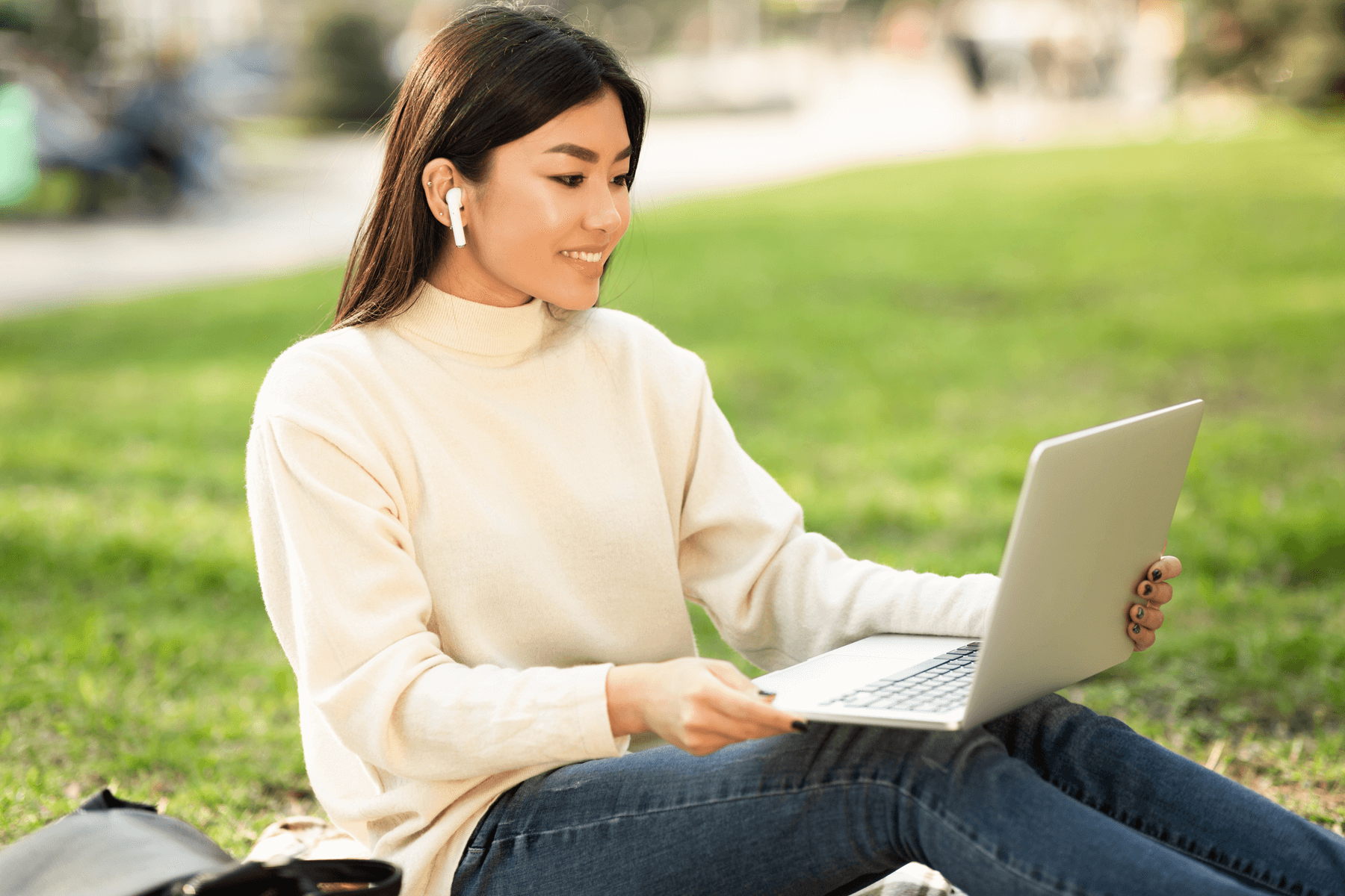 female student on laptop outside in grass with wireless earbuds for school