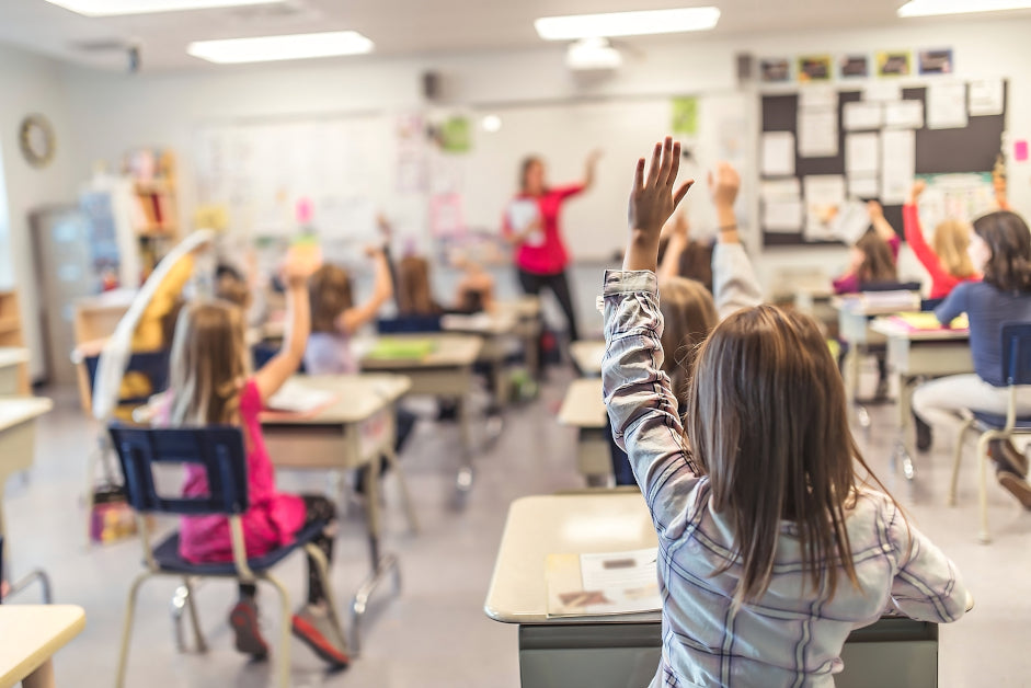 Elementary classroom with students raising their hands at their desks