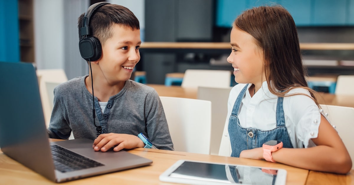 Two students using school headphones while sharing a laptop in a classroom learning environment.