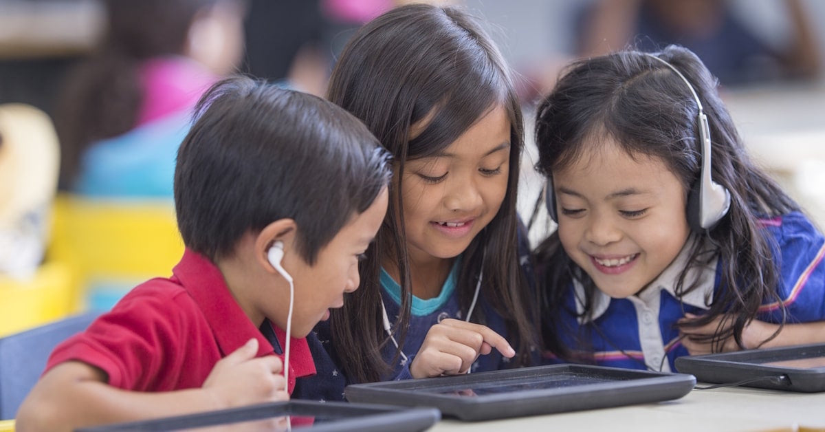 Students at desk with headphones and earbuds. School earbuds vs. school headphones – what’s the difference? Our article breaks down the five major factors to consider when purchasing new school headphones or headsets.