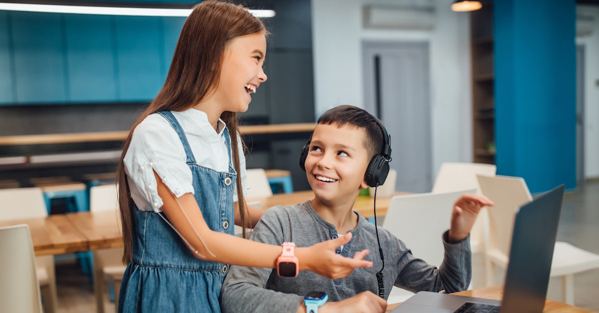 student wearing headphones with another student engaged not wearing school headphones and smiling together at a laptop