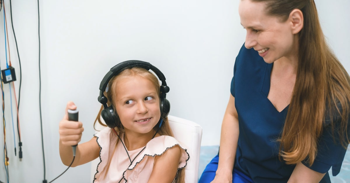 Child wearing over-ear headphones with adult supervision during a speech-focused educational activity