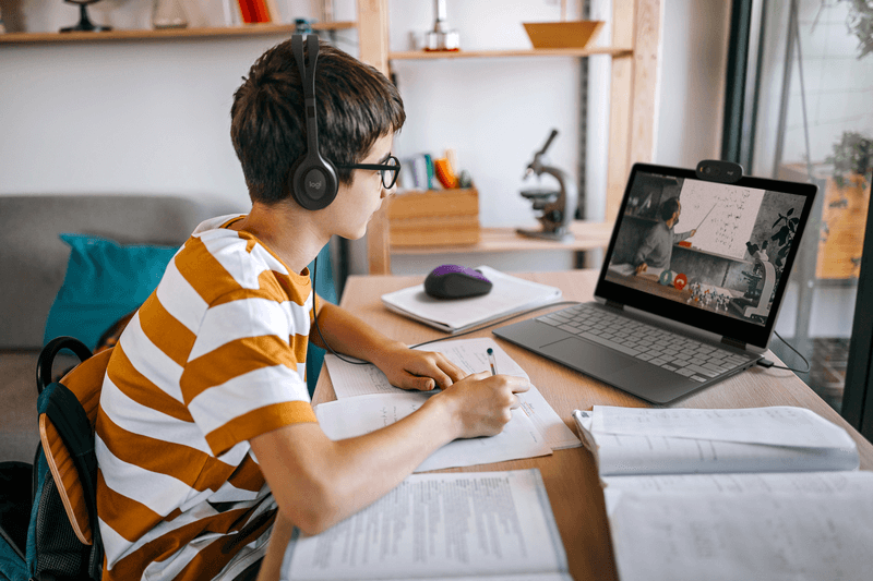 Student wearing Logitech H111 headset for education, engaged in remote learning with laptop and study materials.