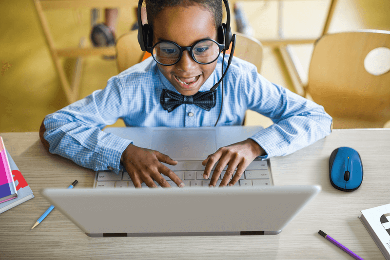 Happy child wearing Logitech H111 headset while studying on a laptop, ideal for school headphones and education.